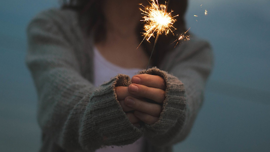 Girl in a sweater holding a sparkler.